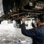 Recall da Volkswagen: mecânico inspeciona componentes e parafusos da caixa de direção sob um carro erguido em oficina.