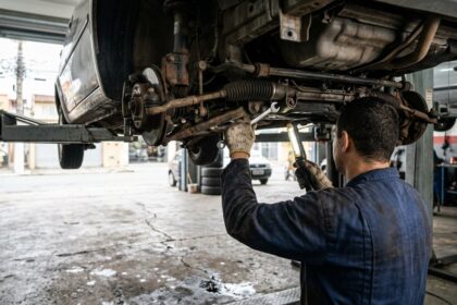 Recall da Volkswagen: mec&acirc;nico inspeciona componentes e parafusos da caixa de dire&ccedil;&atilde;o sob um carro erguido em oficina.