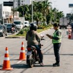 Regras para ciclomotores: ciclomotor parado em fiscalização de trânsito em avenida brasileira, com condutor de capacete segurando documento.